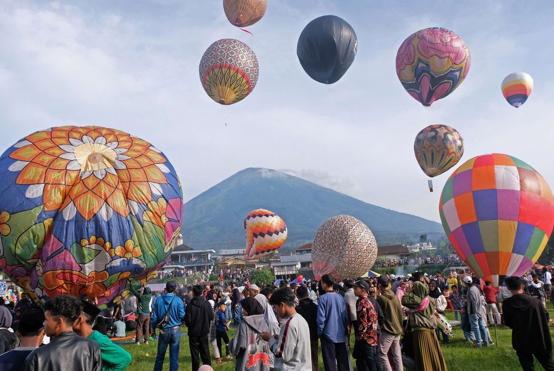 Festival balon udara Wonosobo dengan latar pegunungan dan keramaian pengunjung di lapangan terbuka.